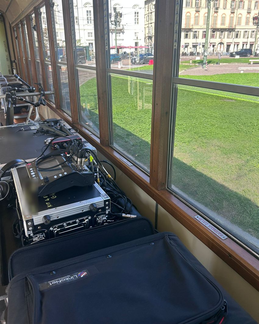 La postazione di regia audio e video a bordo del tram, accanto alla borsa del kit LinkoNet, con la piazza che scorre dal finestrino